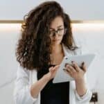 A woman uses a tablet in a modern kitchen, focusing on technology and multitasking.