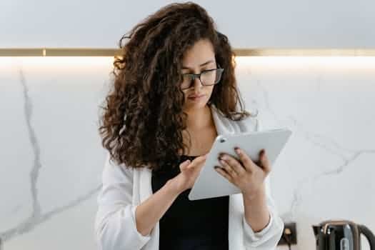 A woman uses a tablet in a modern kitchen, focusing on technology and multitasking.